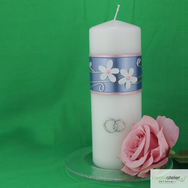 Hochzeitskerze mit weißen Blumen, blauem Band und Ringen